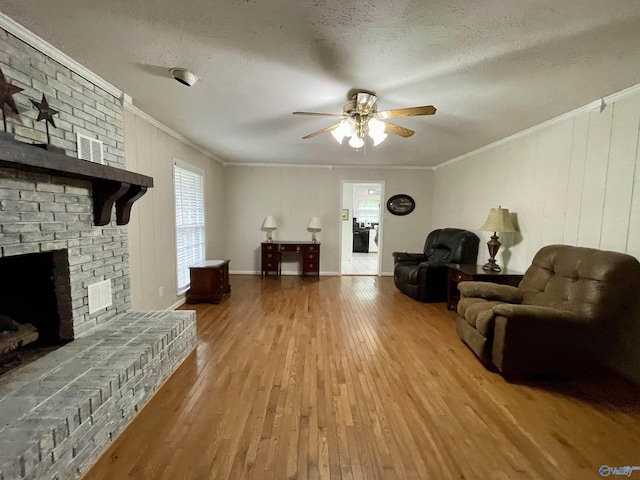 living area with wood finished floors, a ceiling fan, a fireplace, crown molding, and a textured ceiling