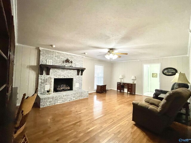 living room featuring wood finished floors, a ceiling fan, a fireplace, crown molding, and a textured ceiling