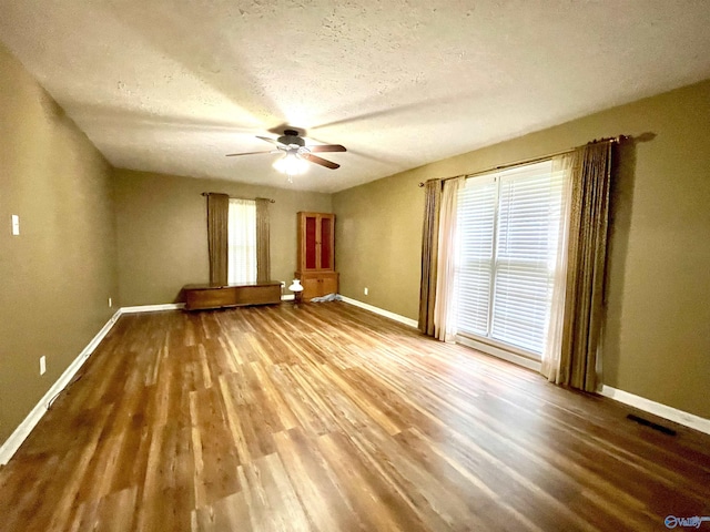 spare room with wood finished floors, baseboards, a ceiling fan, and a textured ceiling