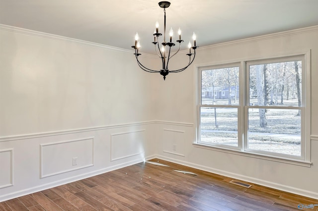 spare room featuring a notable chandelier, plenty of natural light, wood-type flooring, and crown molding