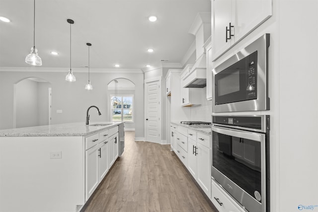 kitchen featuring a center island with sink, hanging light fixtures, light stone countertops, sink, and white cabinetry