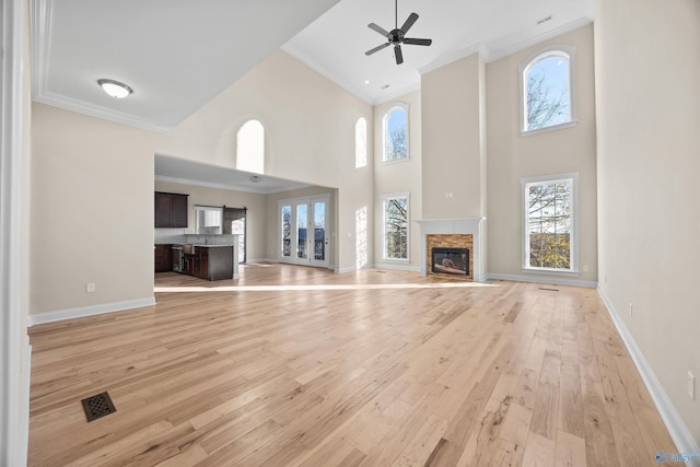 unfurnished living room featuring ornamental molding, a towering ceiling, light hardwood / wood-style flooring, and a stone fireplace