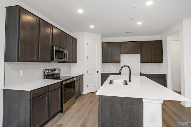 kitchen with sink, light hardwood / wood-style flooring, appliances with stainless steel finishes, a kitchen island with sink, and dark brown cabinets