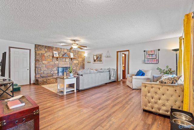 living room featuring a stone fireplace, a textured ceiling, wood-type flooring, and ceiling fan