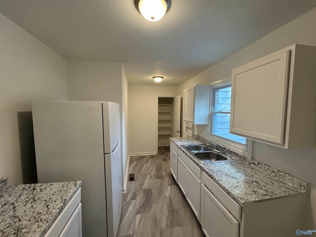 kitchen with sink, light stone counters, light hardwood / wood-style flooring, white refrigerator, and white cabinets