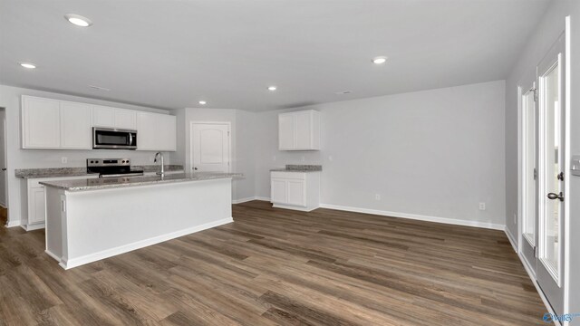 kitchen with light stone countertops, appliances with stainless steel finishes, dark hardwood / wood-style flooring, white cabinetry, and an island with sink