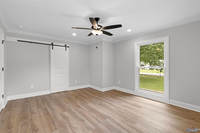 unfurnished room with light wood-type flooring, a ceiling fan, ornamental molding, a barn door, and baseboards