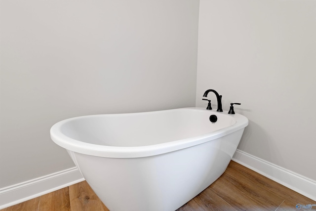 full bath with baseboards, a freestanding bath, and wood finished floors