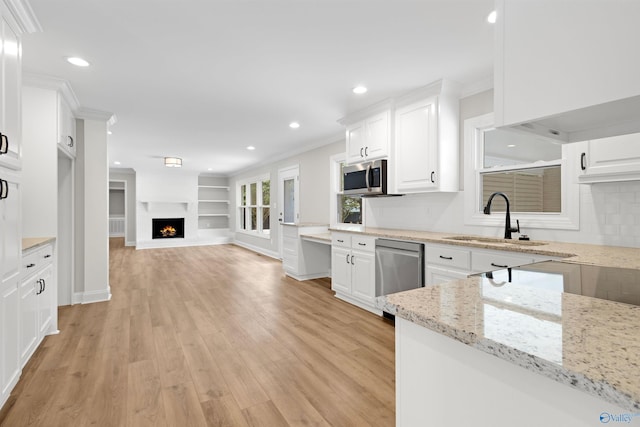 kitchen featuring a sink, appliances with stainless steel finishes, white cabinets, ornamental molding, and light wood-style floors