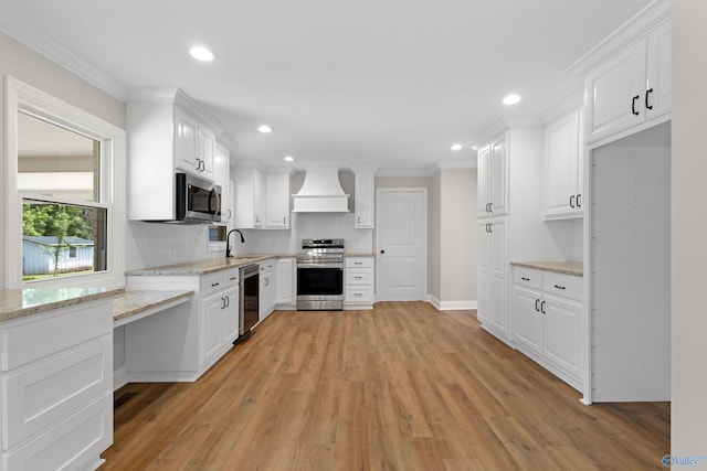 kitchen featuring appliances with stainless steel finishes, custom exhaust hood, white cabinets, light wood-type flooring, and crown molding