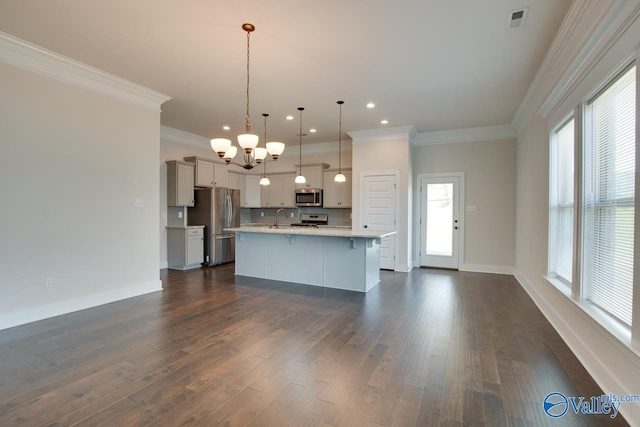 kitchen featuring dark wood-type flooring, decorative light fixtures, a center island with sink, and stainless steel appliances