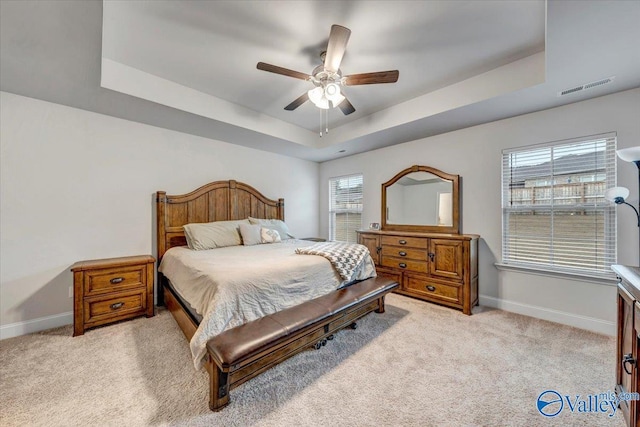 bedroom with light carpet, visible vents, baseboards, and a tray ceiling