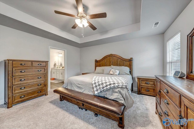 bedroom featuring visible vents, a raised ceiling, light carpet, and connected bathroom