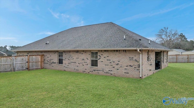 rear view of property featuring brick siding, a fenced backyard, a lawn, and roof with shingles