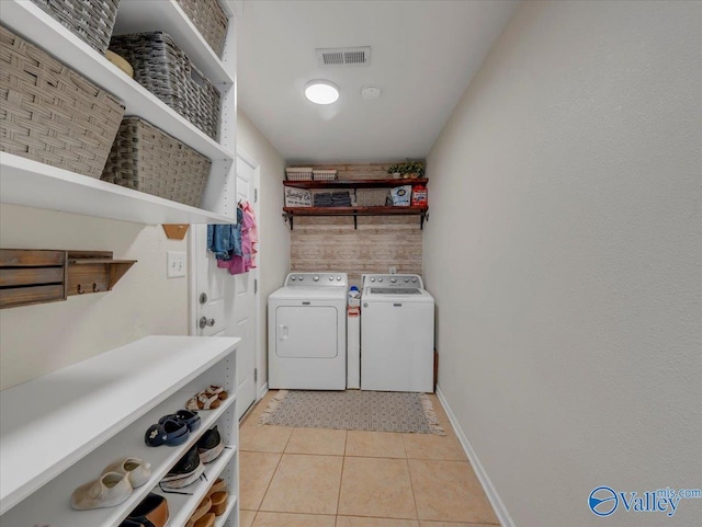 clothes washing area with baseboards, light tile patterned floors, washing machine and dryer, visible vents, and laundry area