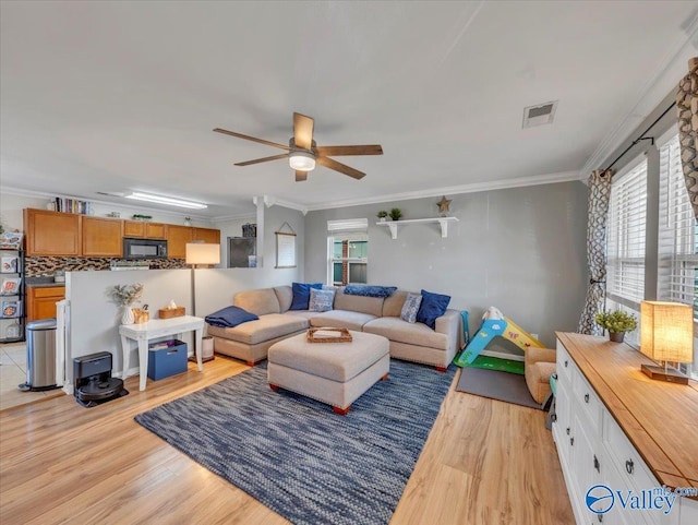 living area with ornamental molding, visible vents, light wood-type flooring, and a ceiling fan