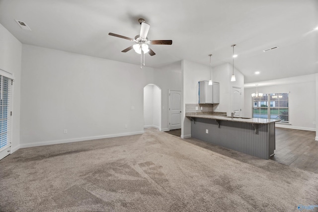 kitchen featuring a kitchen breakfast bar, arched walkways, baseboards, ceiling fan with notable chandelier, and lofted ceiling