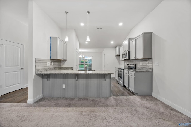 kitchen with dark colored carpet, a peninsula, appliances with stainless steel finishes, and backsplash