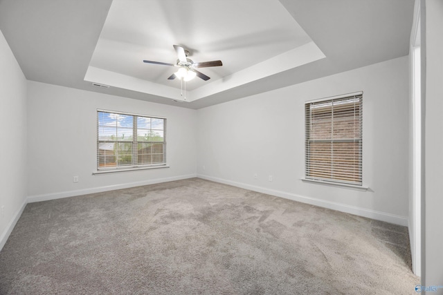 spare room with a raised ceiling, carpet floors, a ceiling fan, baseboards, and visible vents