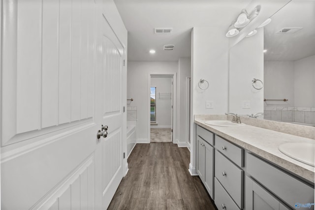 full bathroom with a tub, double vanity, visible vents, wood finished floors, and a sink