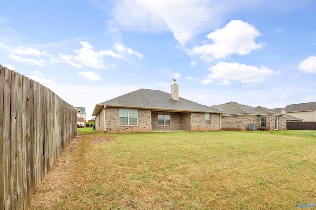 back of house featuring brick siding, fence, a yard, and a chimney