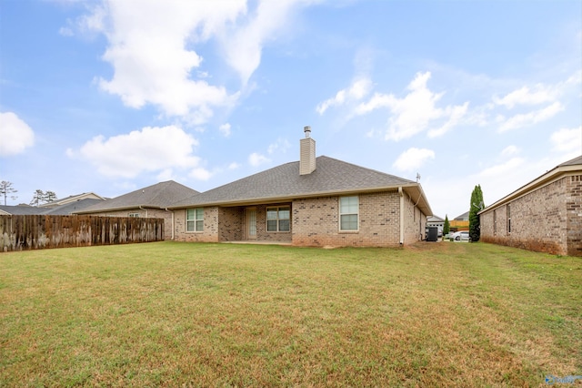 back of house featuring a lawn, brick siding, fence, and a chimney