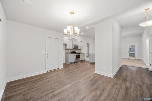 unfurnished living room with an inviting chandelier, baseboards, dark wood-type flooring, recessed lighting, and arched walkways