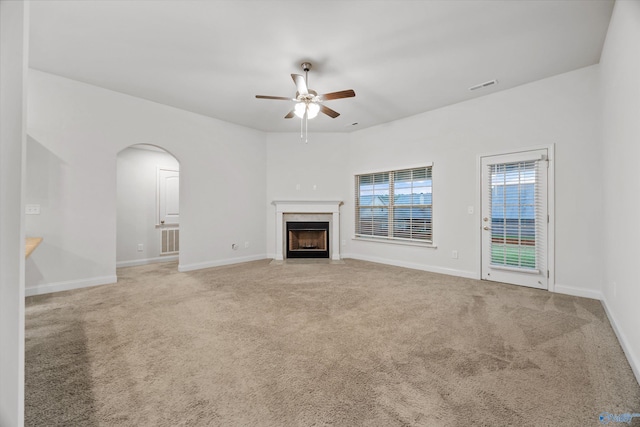 unfurnished living room featuring a ceiling fan, visible vents, a tiled fireplace, arched walkways, and carpet flooring