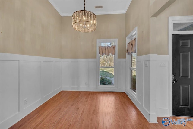 interior space with a decorative wall, visible vents, a chandelier, crown molding, and wood finished floors