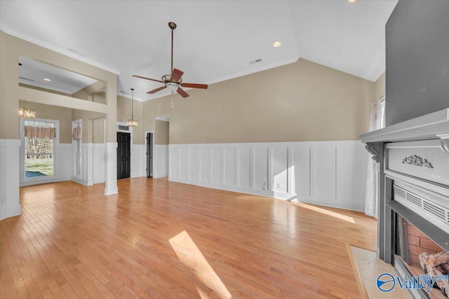 unfurnished living room featuring a fireplace with flush hearth, lofted ceiling, light wood-type flooring, ceiling fan with notable chandelier, and wainscoting