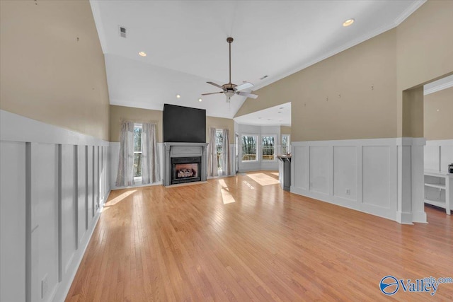 unfurnished living room with a decorative wall, light wood finished floors, a fireplace, a ceiling fan, and wainscoting