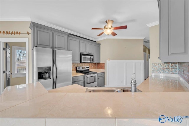 kitchen with gray cabinets, ornamental molding, a sink, a ceiling fan, and appliances with stainless steel finishes