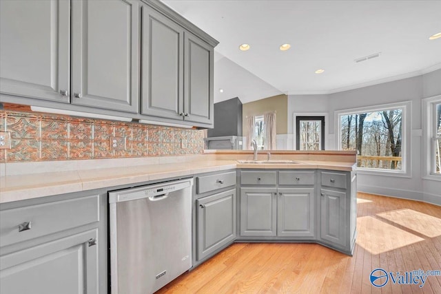 kitchen with light countertops, gray cabinets, stainless steel dishwasher, a sink, and visible vents