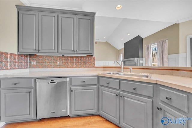 kitchen with gray cabinets, light countertops, vaulted ceiling, a sink, and stainless steel dishwasher