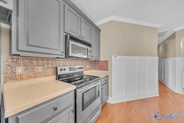 kitchen with gray cabinets, light countertops, light wood-style flooring, stainless steel appliances, and ornamental molding