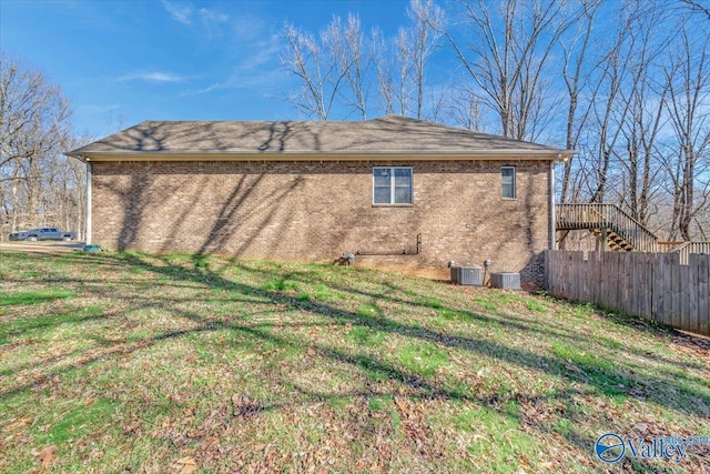 view of side of home featuring central AC unit, fence, stairway, brick siding, and a yard