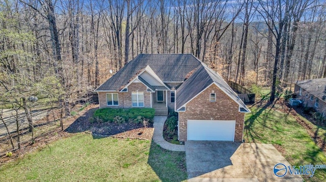 view of front facade featuring driveway, brick siding, a wooded view, a front lawn, and a garage