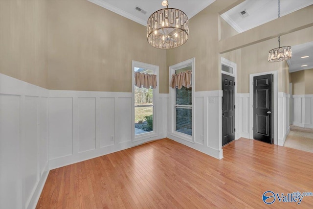 interior space featuring an inviting chandelier, a decorative wall, visible vents, and wood finished floors