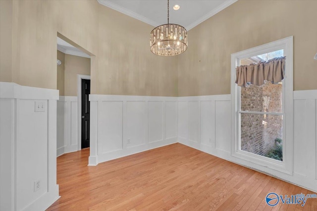 unfurnished room featuring a wainscoted wall, light wood-style floors, ornamental molding, and a chandelier