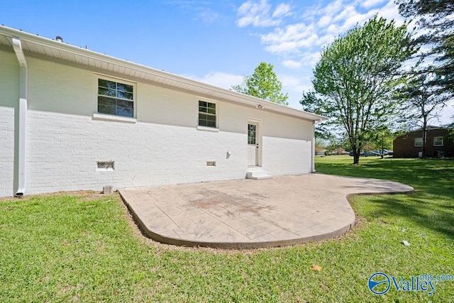 rear view of property featuring a lawn, brick siding, and a patio