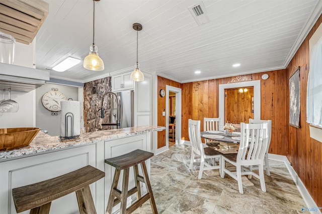 kitchen with stainless steel fridge, white cabinetry, light stone countertops, and wooden walls