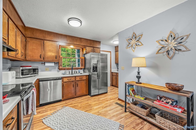 kitchen with sink, a textured ceiling, stainless steel appliances, and light wood-type flooring