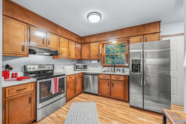 kitchen with appliances with stainless steel finishes, a textured ceiling, sink, and light wood-type flooring