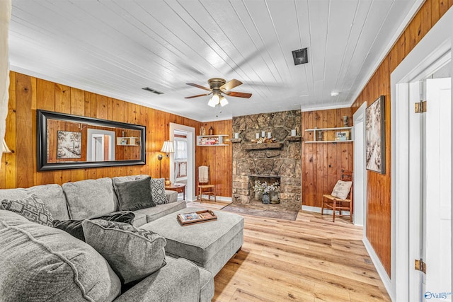 living room featuring wood walls, a fireplace, wood ceiling, ceiling fan, and light hardwood / wood-style flooring