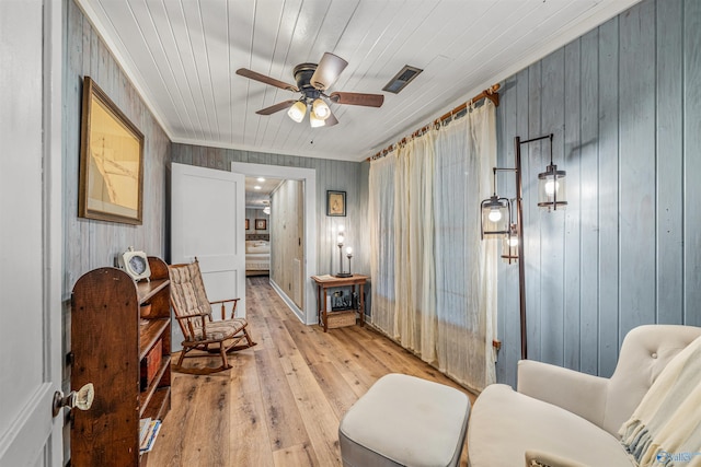 living area with ceiling fan, wooden ceiling, light hardwood / wood-style floors, crown molding, and wooden walls