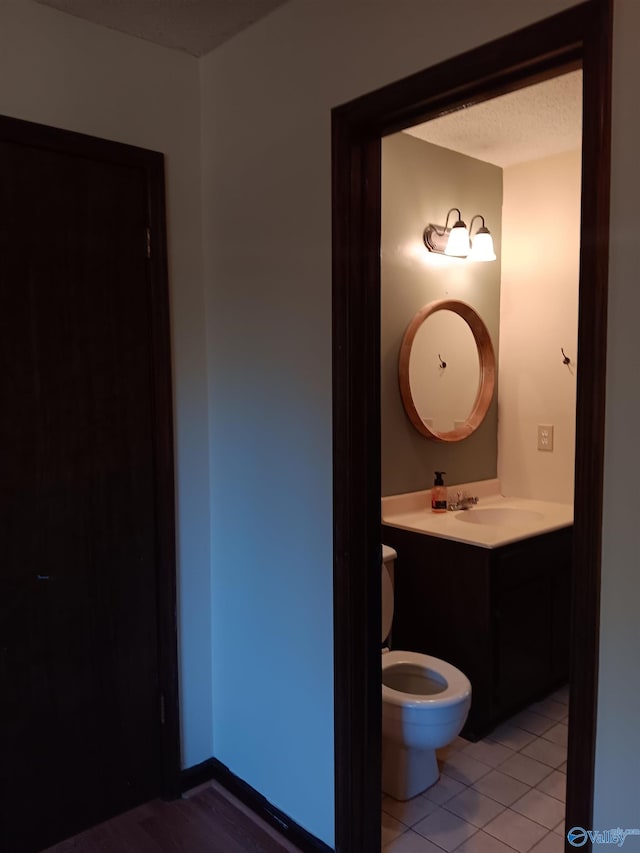 bathroom featuring tile patterned flooring, a textured ceiling, vanity, and toilet