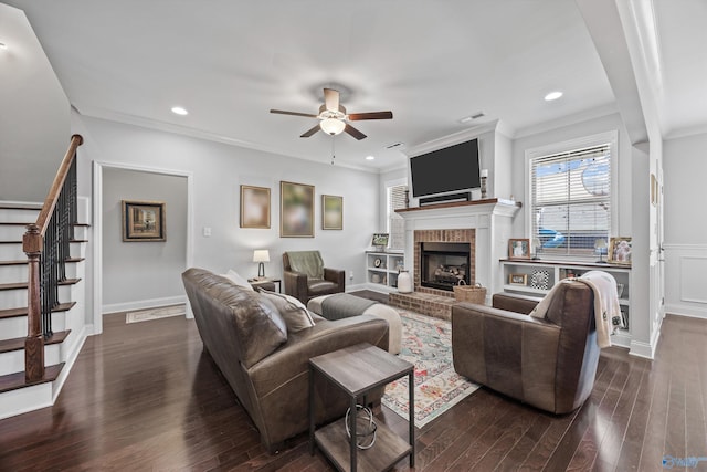 living area with stairway, a ceiling fan, dark wood finished floors, and a brick fireplace