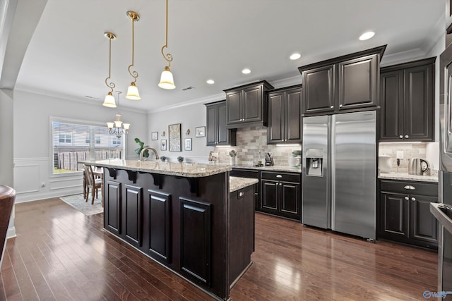 kitchen with crown molding, dark wood-style flooring, an inviting chandelier, stainless steel refrigerator with ice dispenser, and a center island with sink
