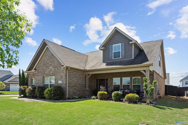 craftsman house with roof with shingles, fence, a front yard, and brick siding
