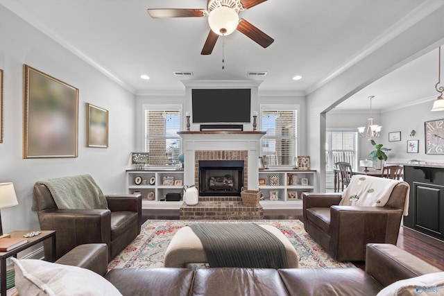 living room featuring visible vents, ornamental molding, ceiling fan with notable chandelier, and wood finished floors